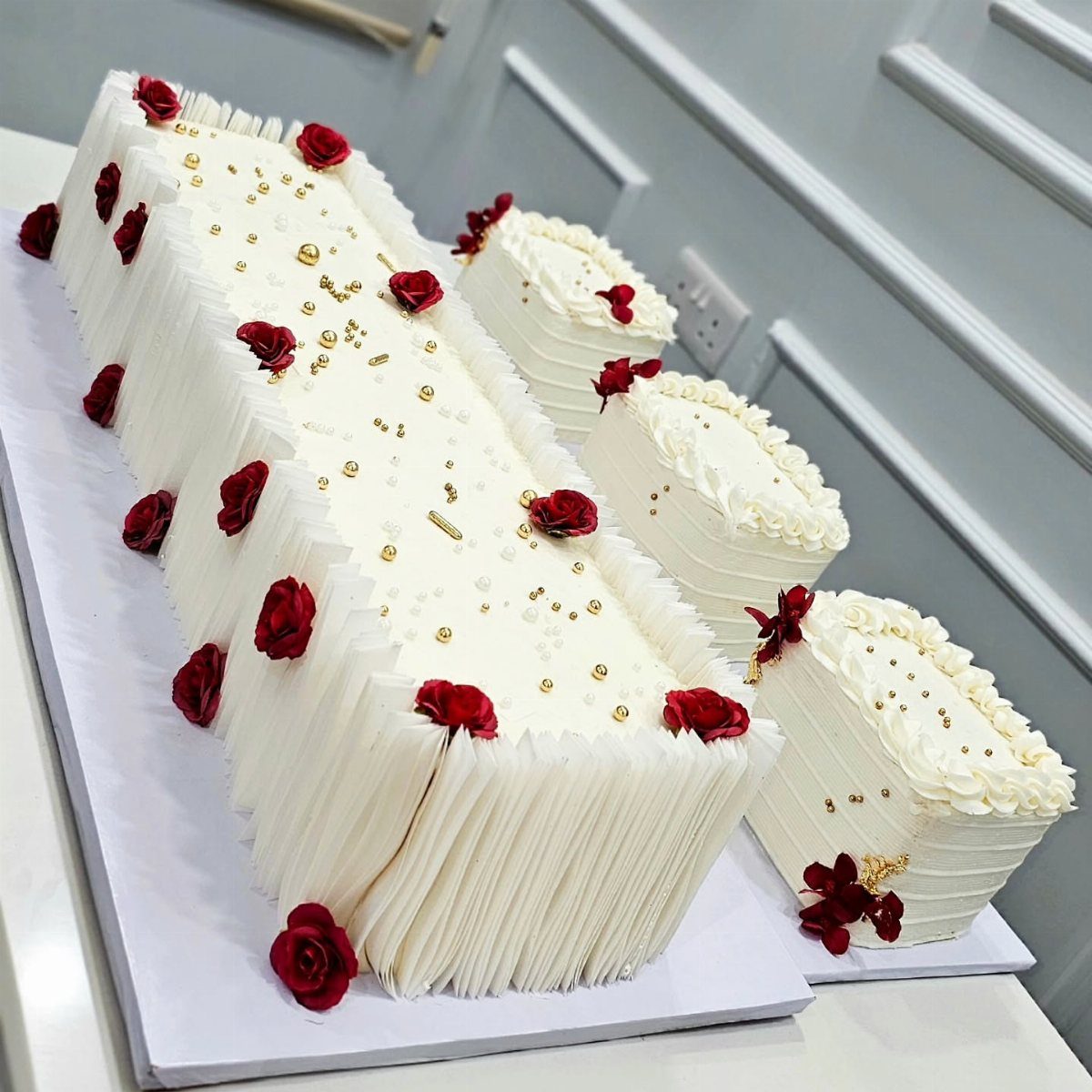 Rectangular white cakes with pleated buttercream sides, gold pearls, and red roses.