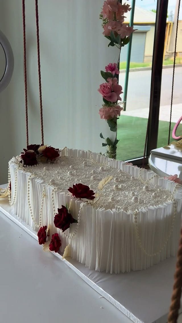 White rectangular wedding cake decorated with red roses and cascading white pearls.