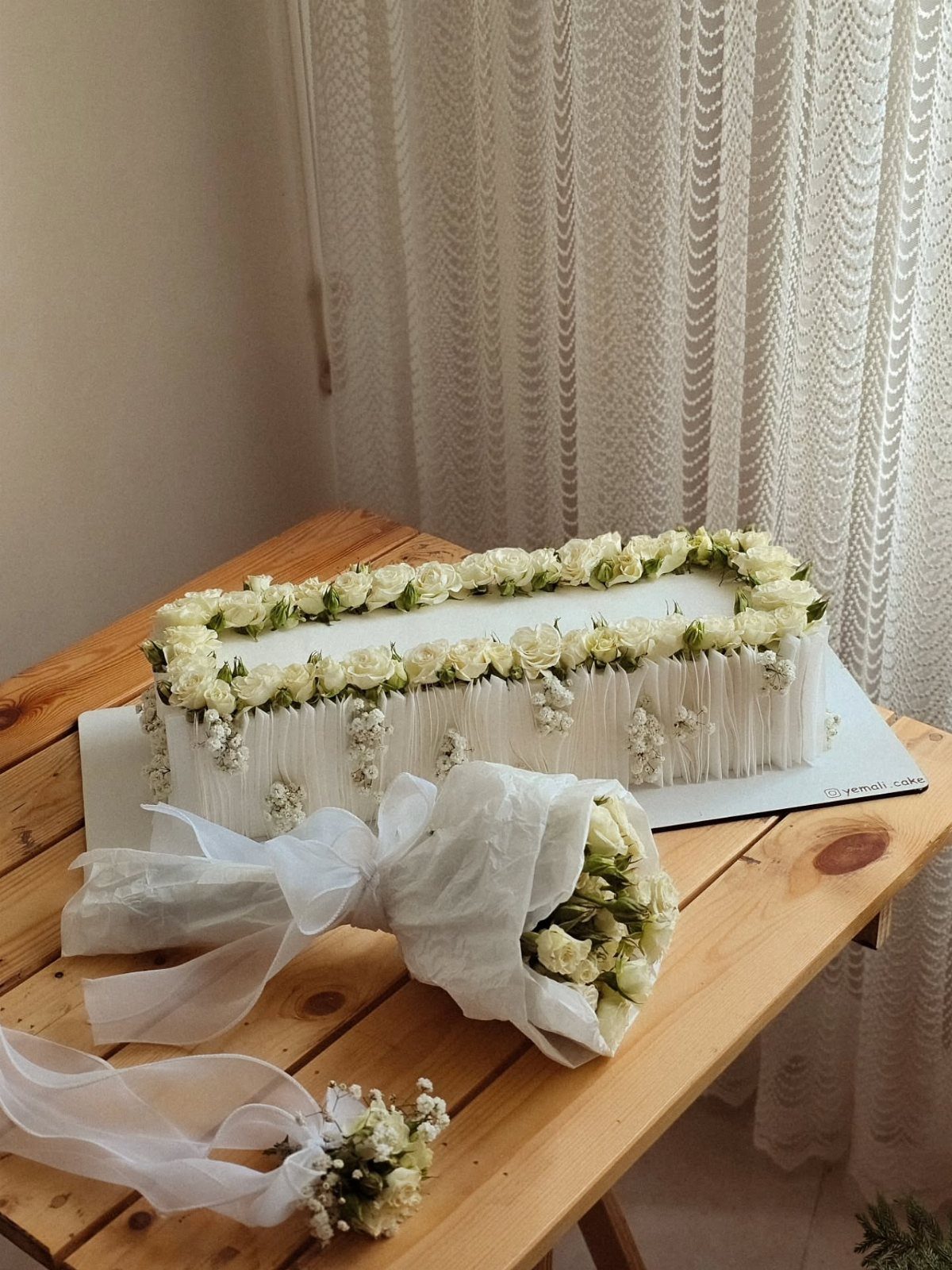Rectangular white wedding cake decorated with white roses on a wooden table.
