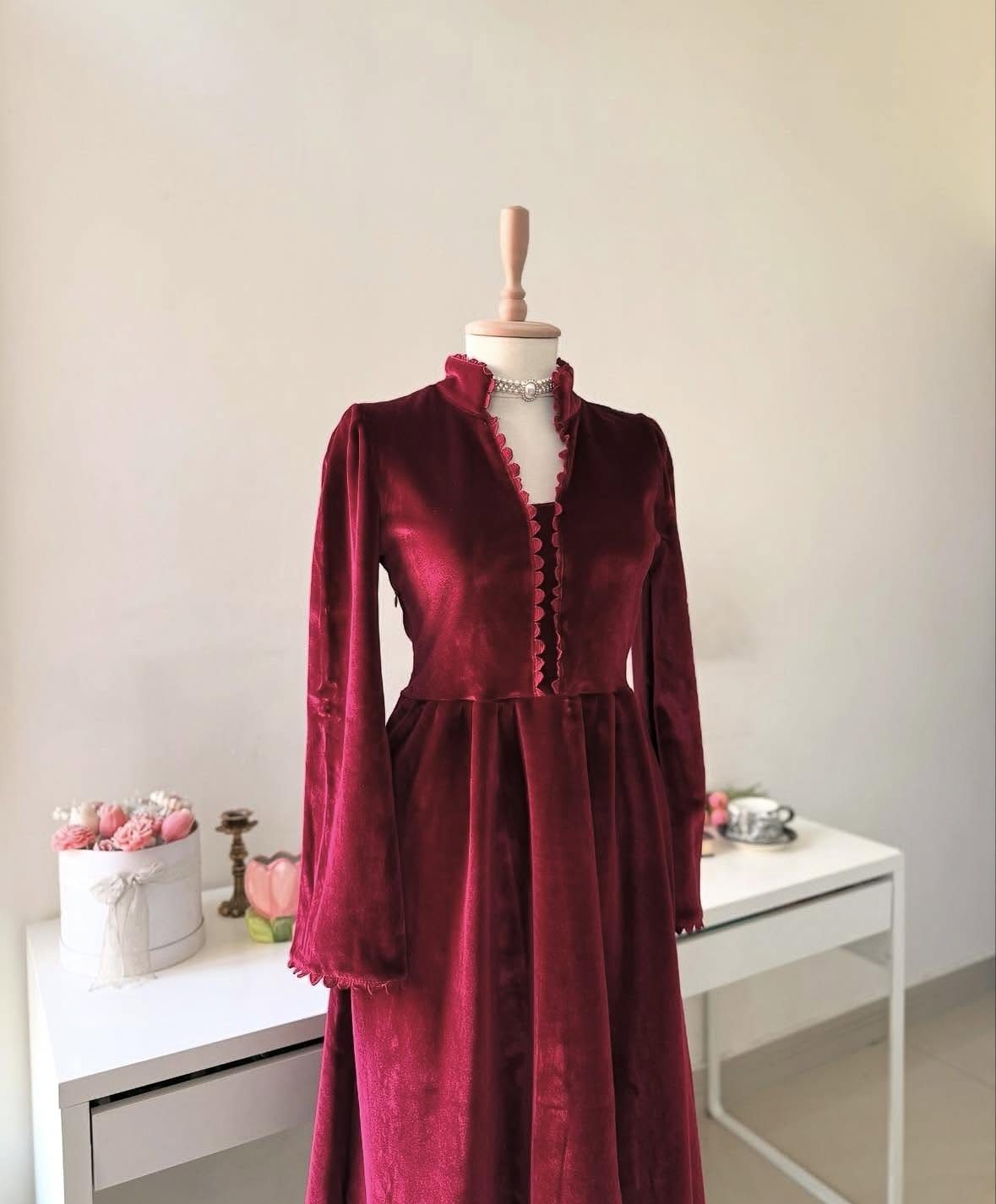 10 Red Wedding Dresses for Brides Who Want Color 6 Deep red velvet long-sleeved dress displayed on a white mannequin in a room.