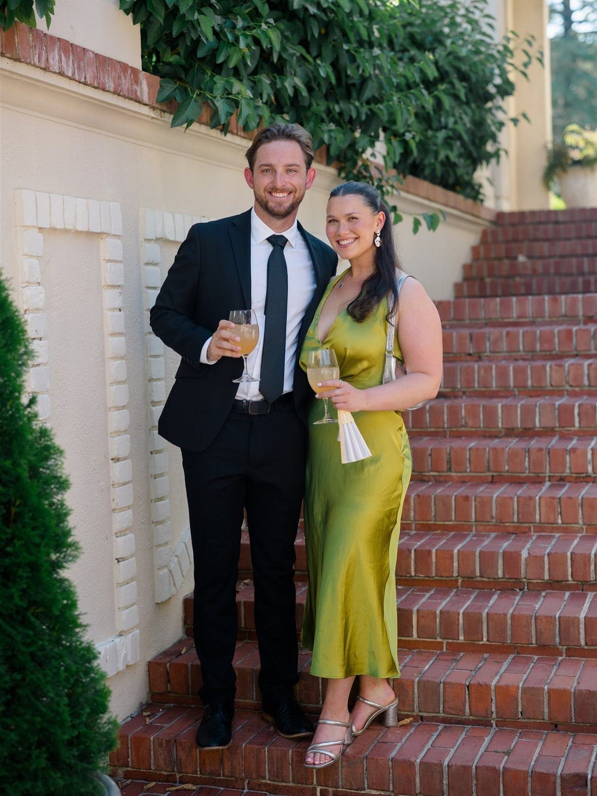 Man in black suit and woman in green satin dress holding champagne glasses.