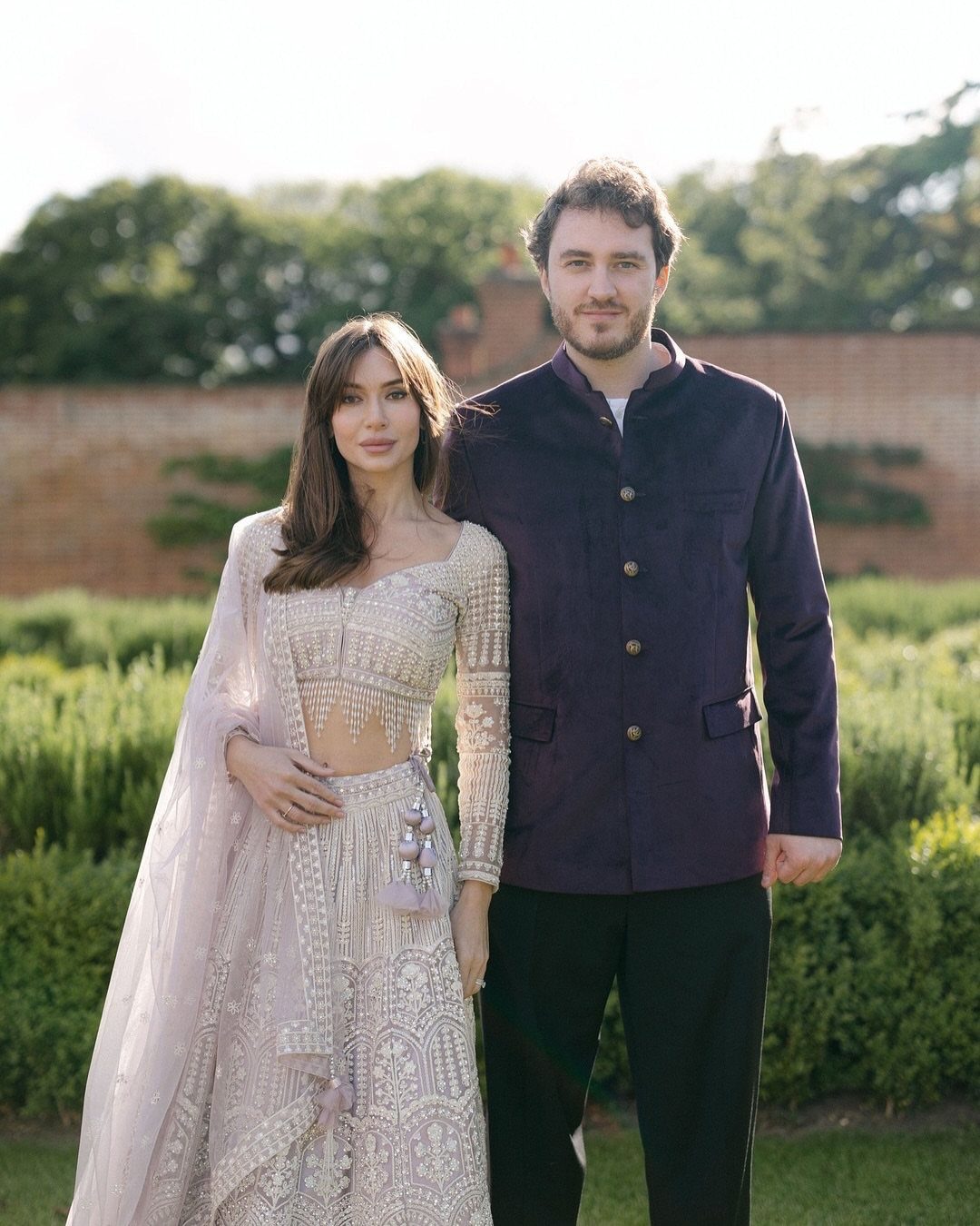 Man and woman in traditional Indian wedding attire posing in a garden setting.