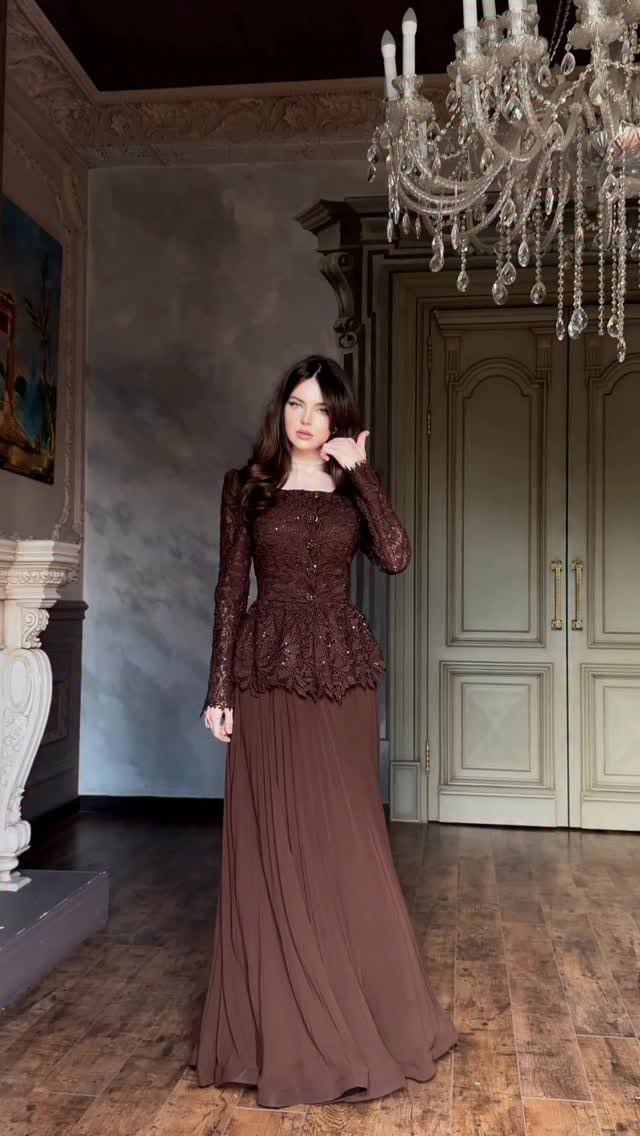Woman wearing a modest long-sleeved brown lace floor-length gown in an ornate room.