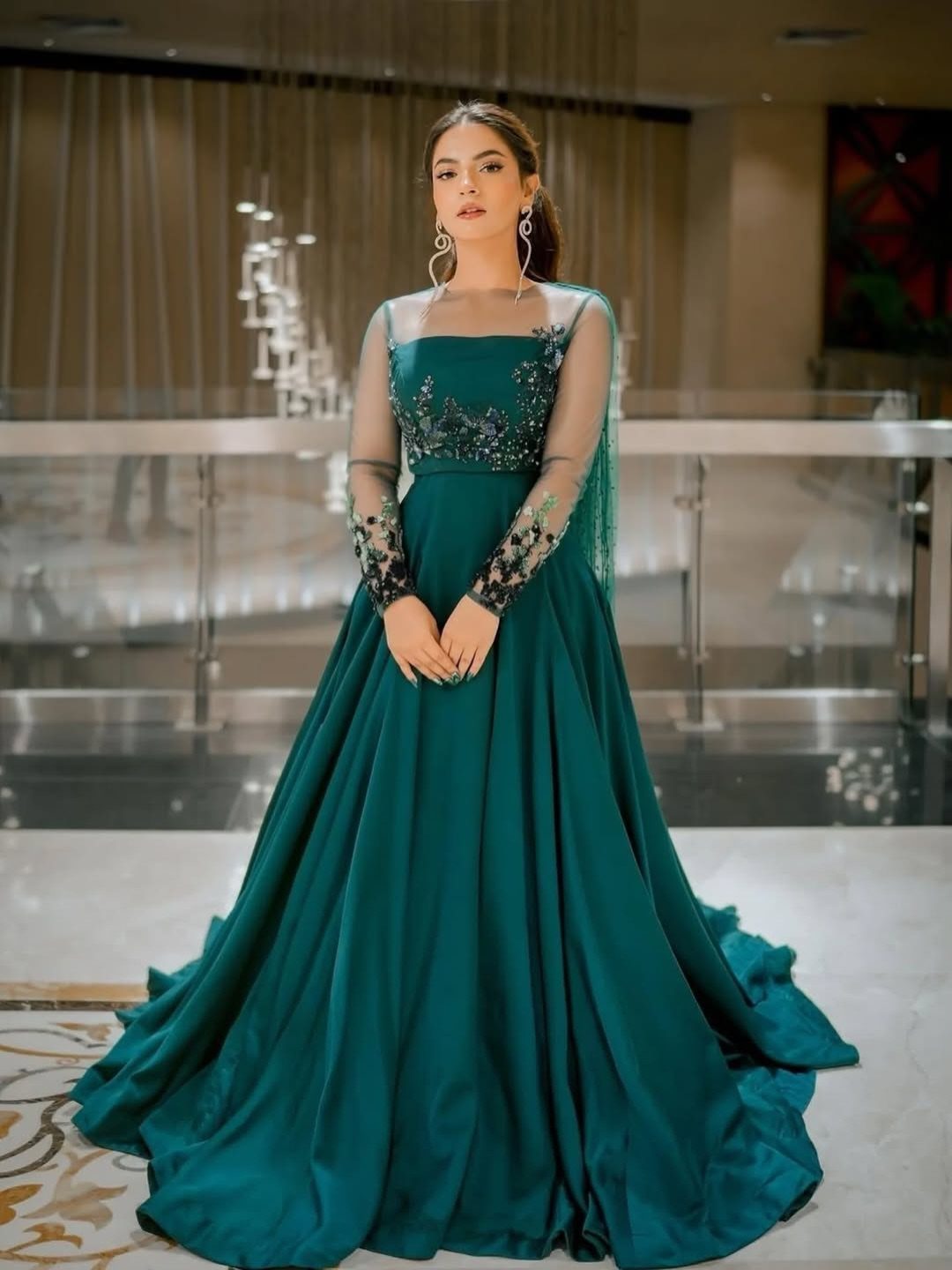 Woman in a formal dark teal floor-length gown with embroidered sheer sleeves.