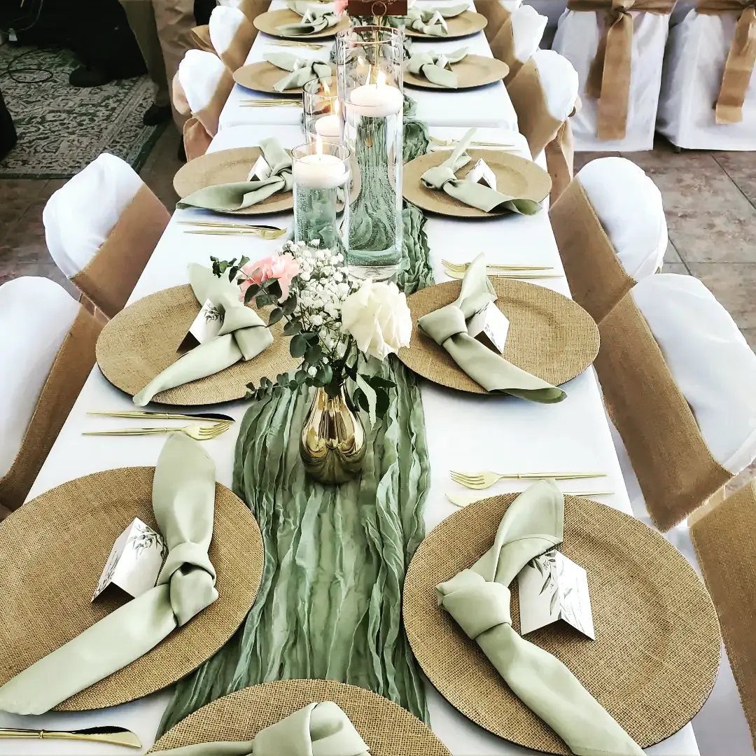 Wedding table setting with sage green runner, gold chargers, and burlap chair sashes.