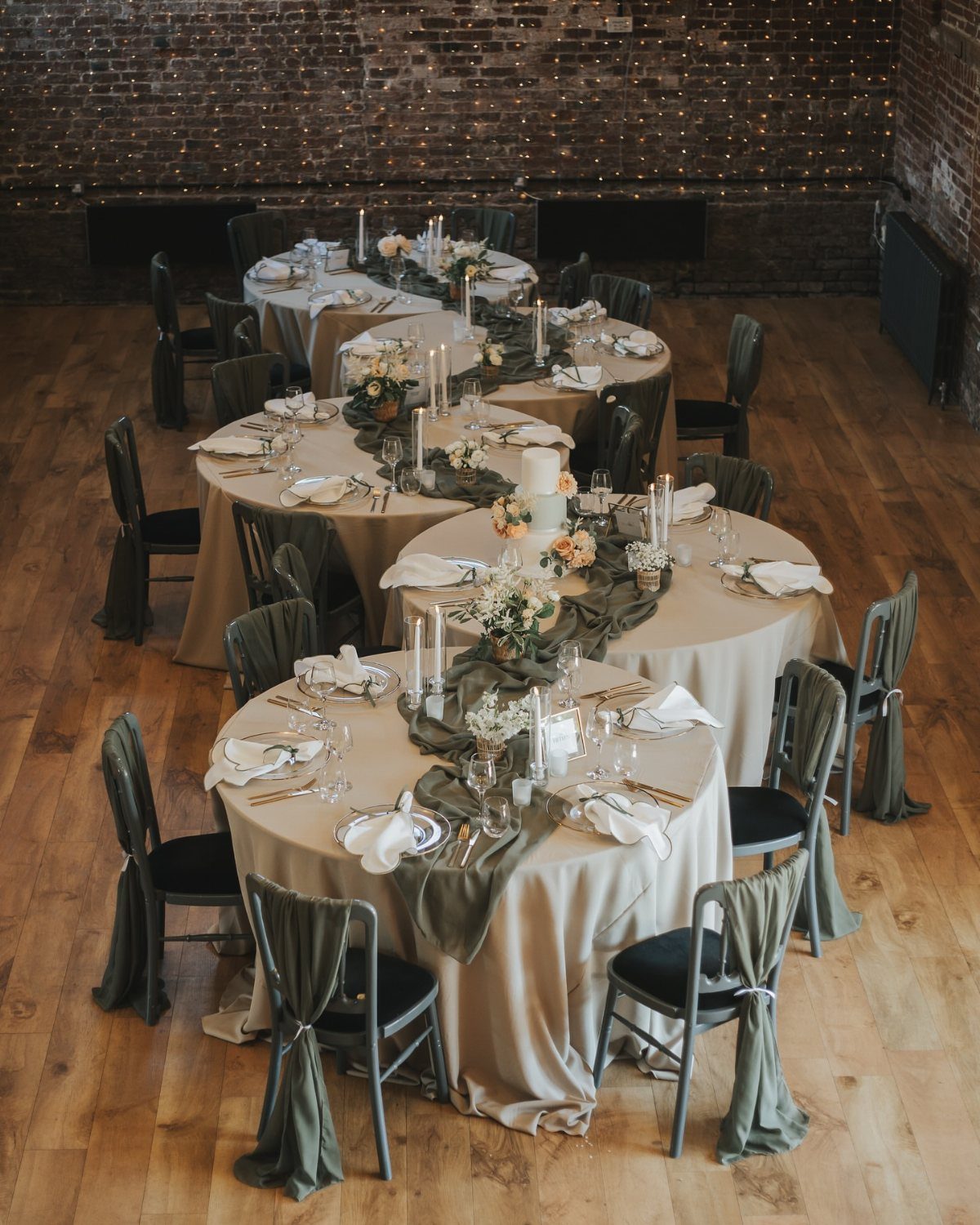 Round wedding tables with beige linens, olive runners, and white taper candles.