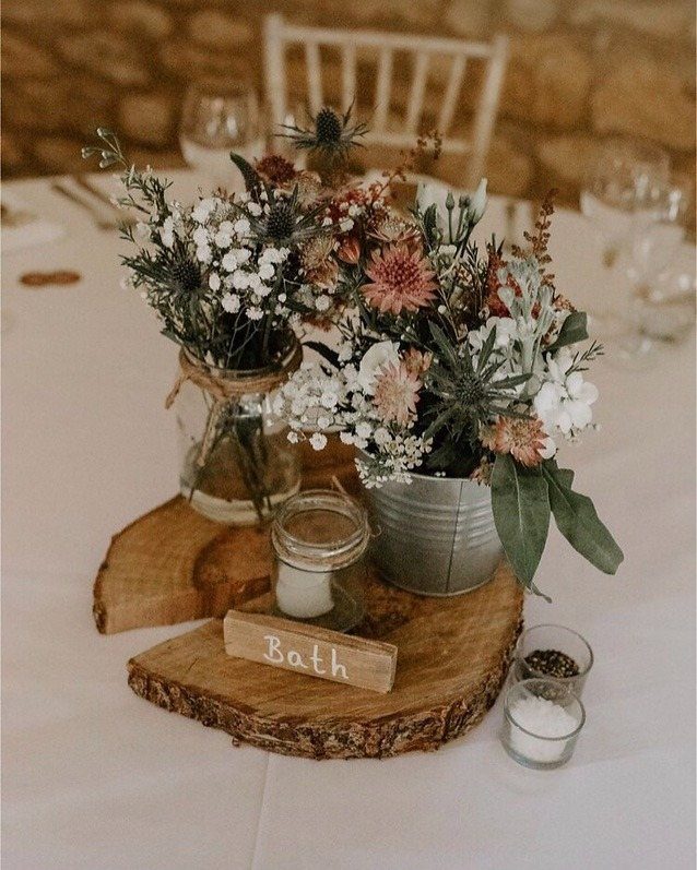 Dried flowers and greenery in rustic containers on wooden slices for a wedding table.