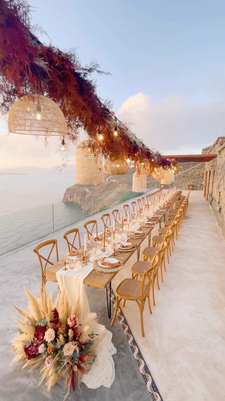 Long wooden wedding table with earthy toned florals and gold chairs overlooking the ocean