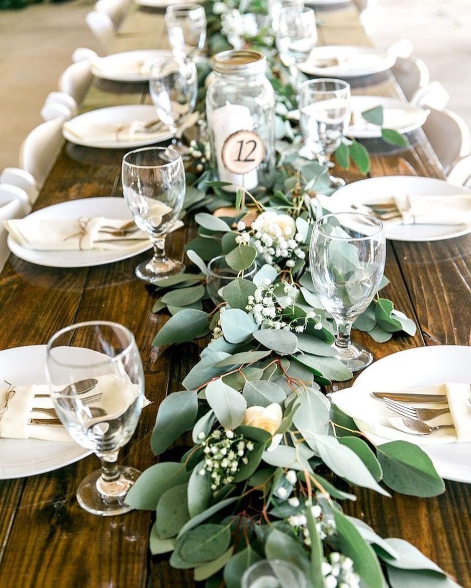 Green eucalyptus garland with white flowers decorating a rustic wooden wedding table setting.