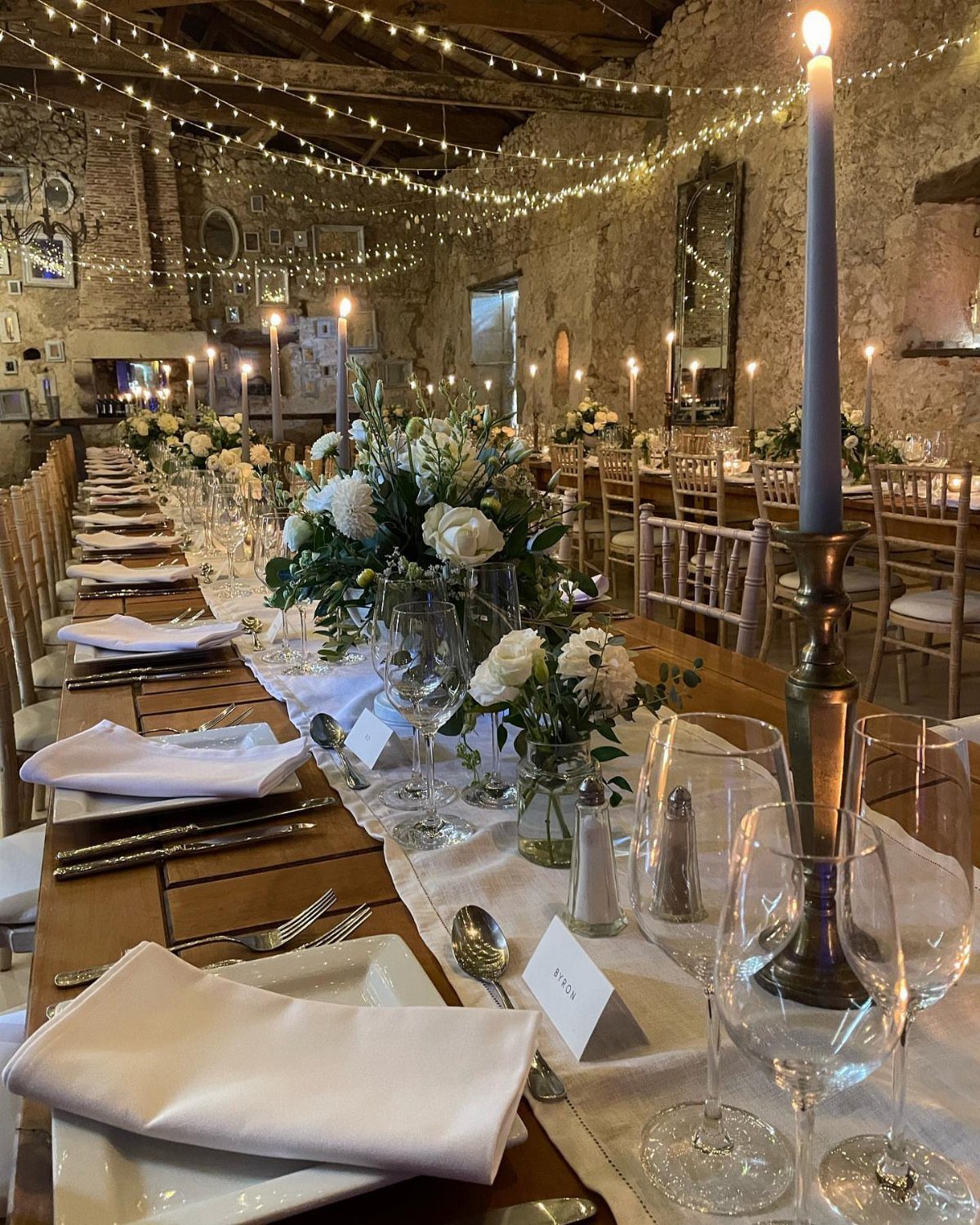 White linen table runner on a wooden wedding table with floral centerpieces and candles.