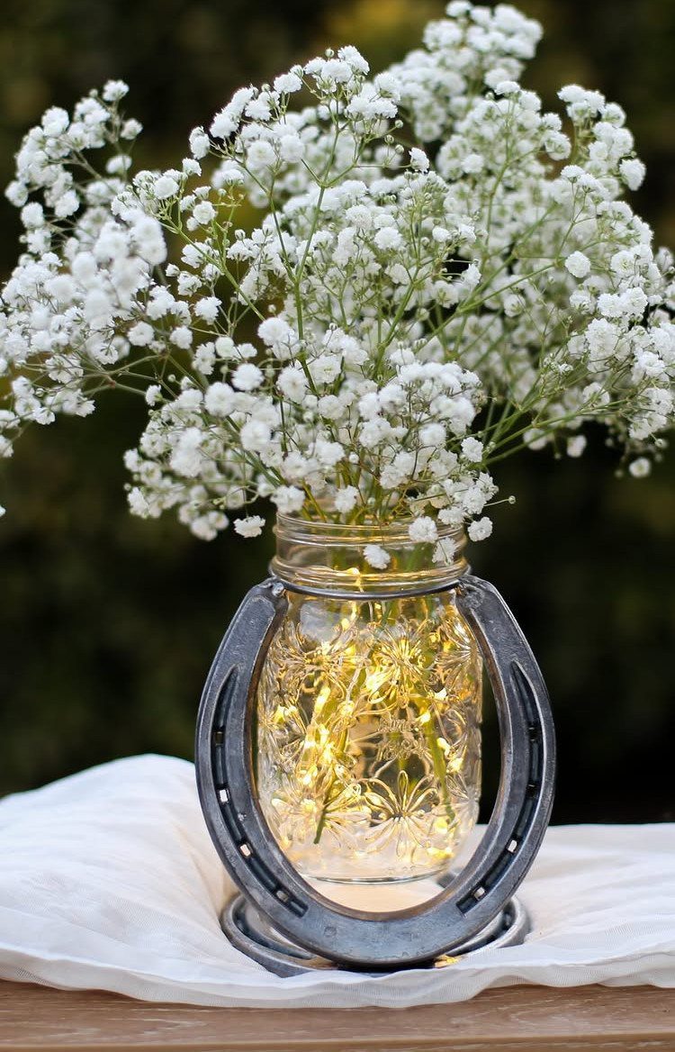 Mason jar with fairy lights and baby's breath flowers inside a metal horseshoe.