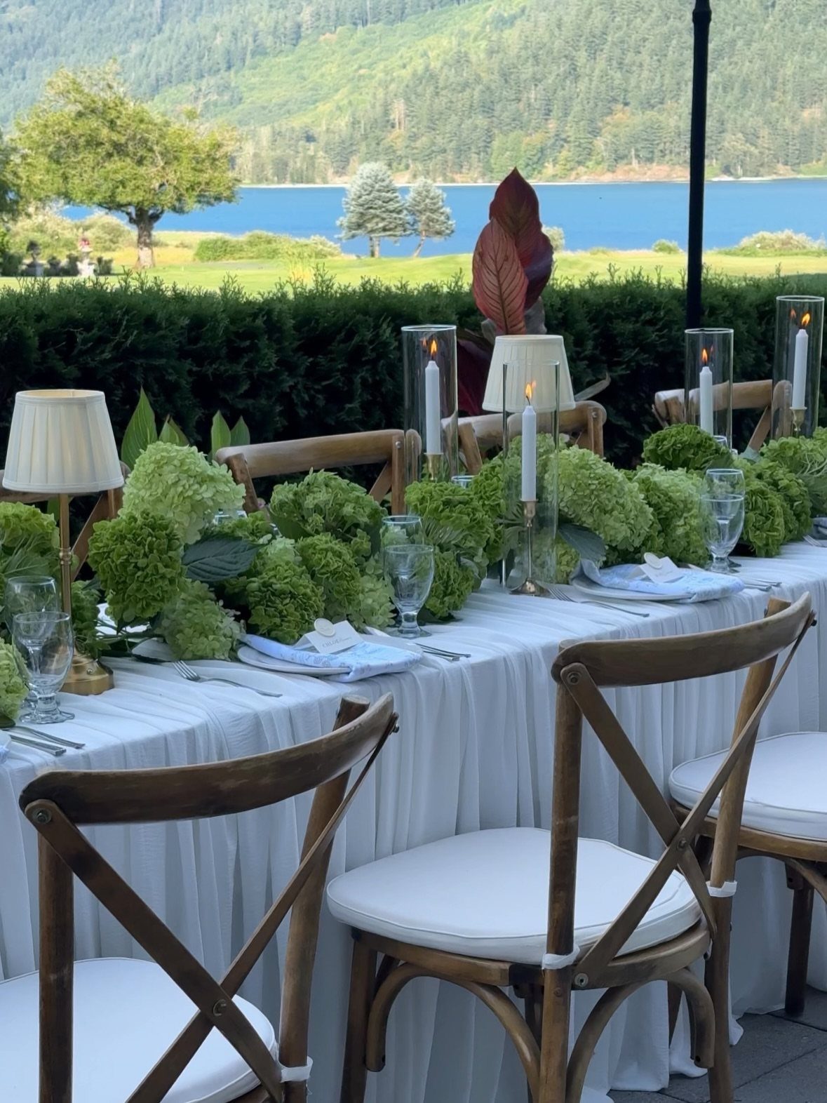 Wedding table with white linens, wooden chairs, and green hydrangea floral centerpieces.
