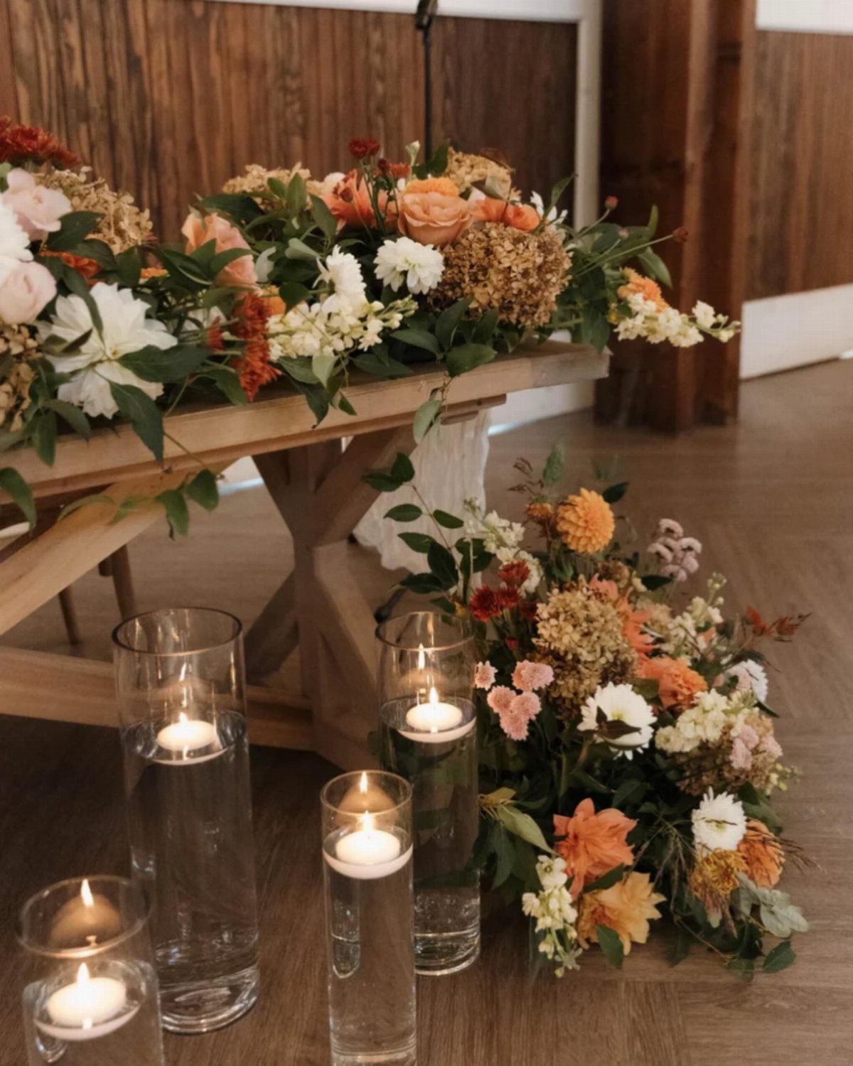 Wildflower-style floral arrangements on a rustic wooden table with floating candles in glass vases.