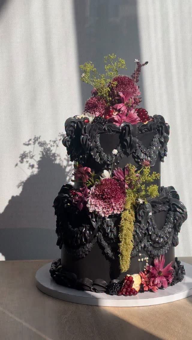 Black three-tier wedding cake with ornate frosting and deep red floral decorations.