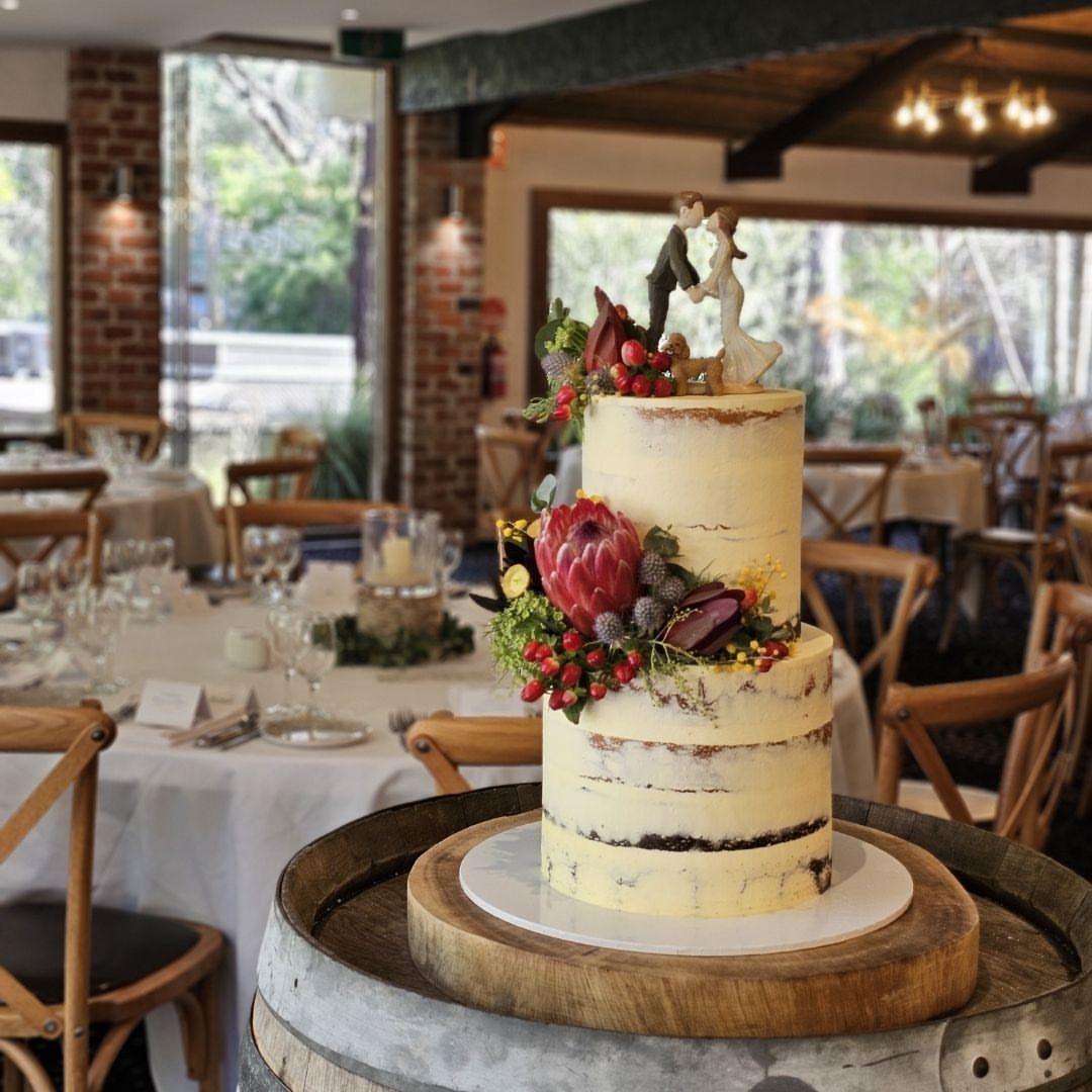 Semi-naked wedding cake with berries and flowers on a wooden barrel stand.