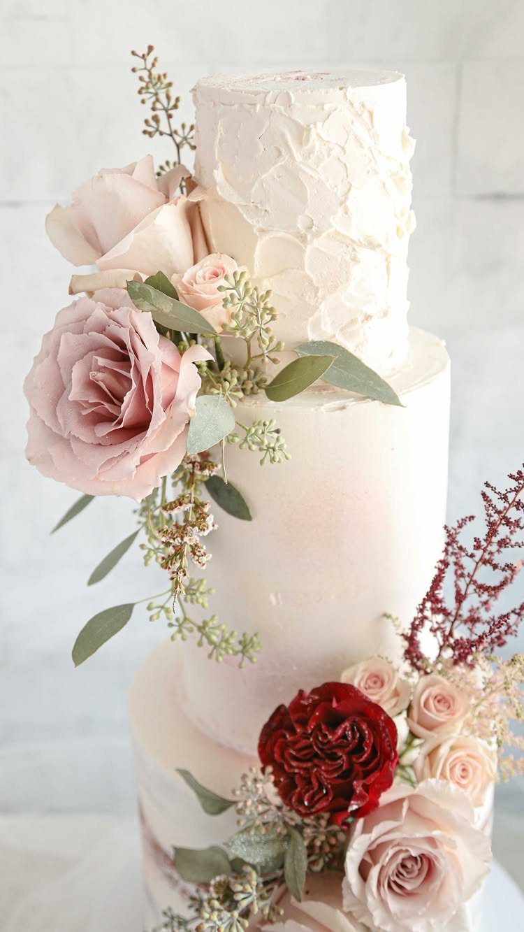 Three-tier white wedding cake with textured frosting and fresh pink and red roses.