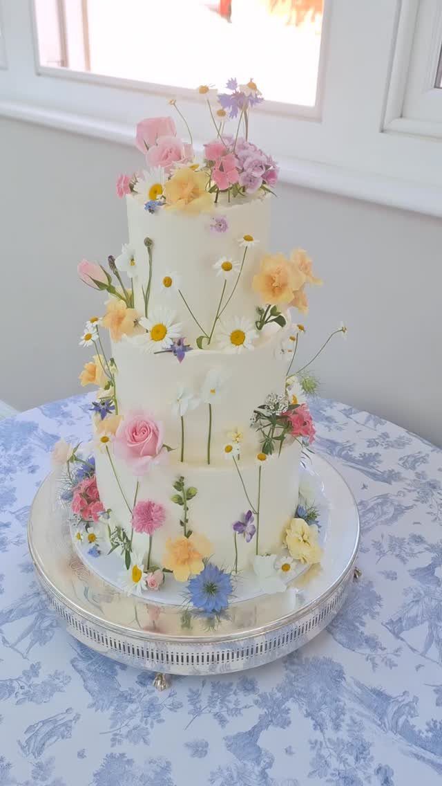 Three-tier white wedding cake decorated with colorful wildflowers on a silver platter.