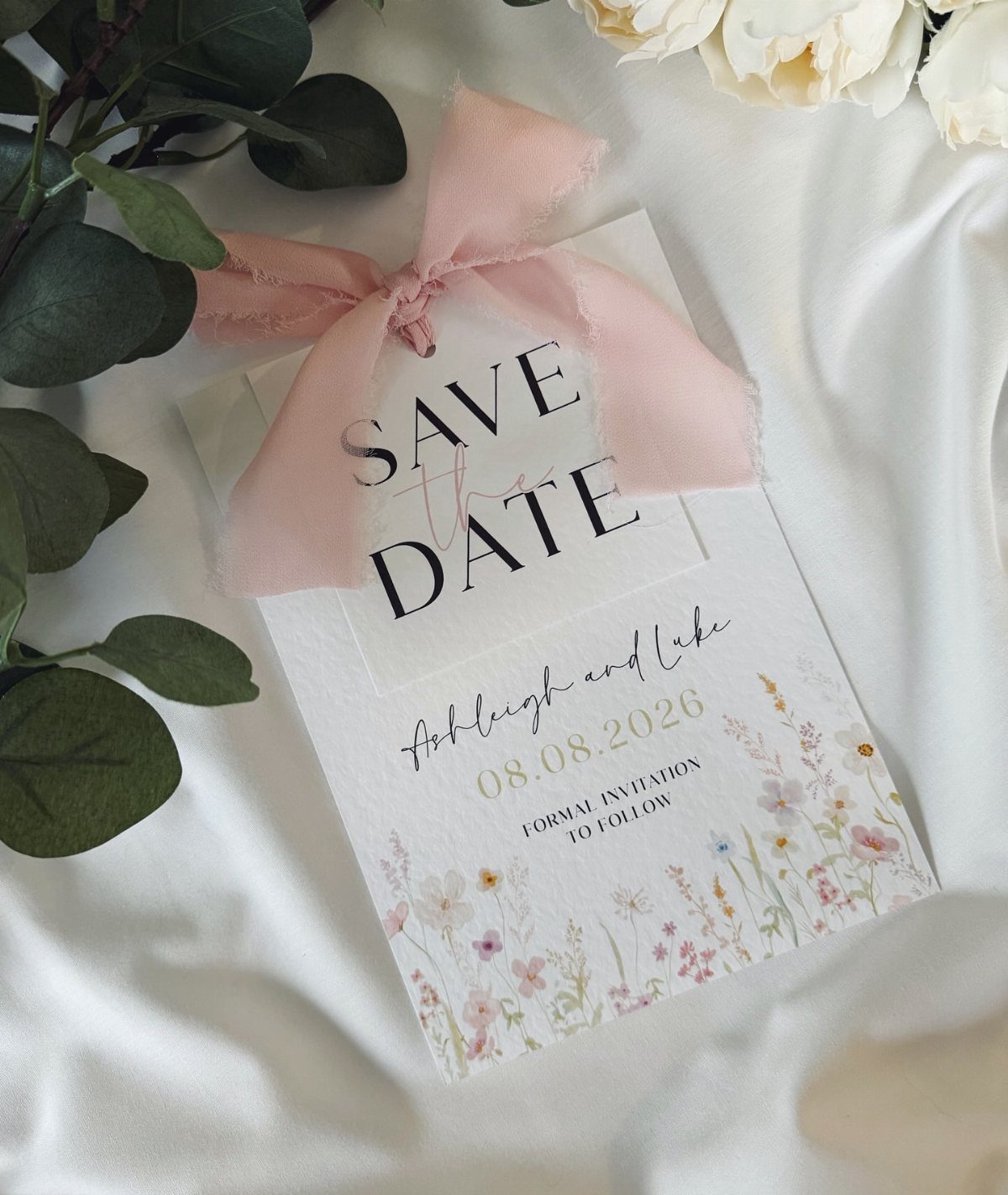 Save the Date Wedding Invite Ideas: 11 Styles to Try 1 Save the date card with pink ribbon and floral illustrations on white satin fabric