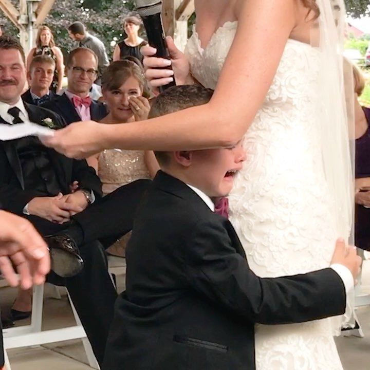 Young boy in a suit hugging a bride in a white lace wedding gown