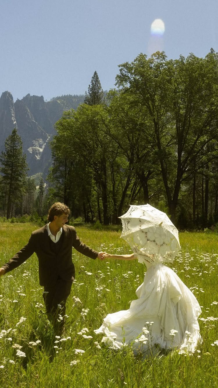 Bride and groom holding hands in a wildflower meadow with mountains in background