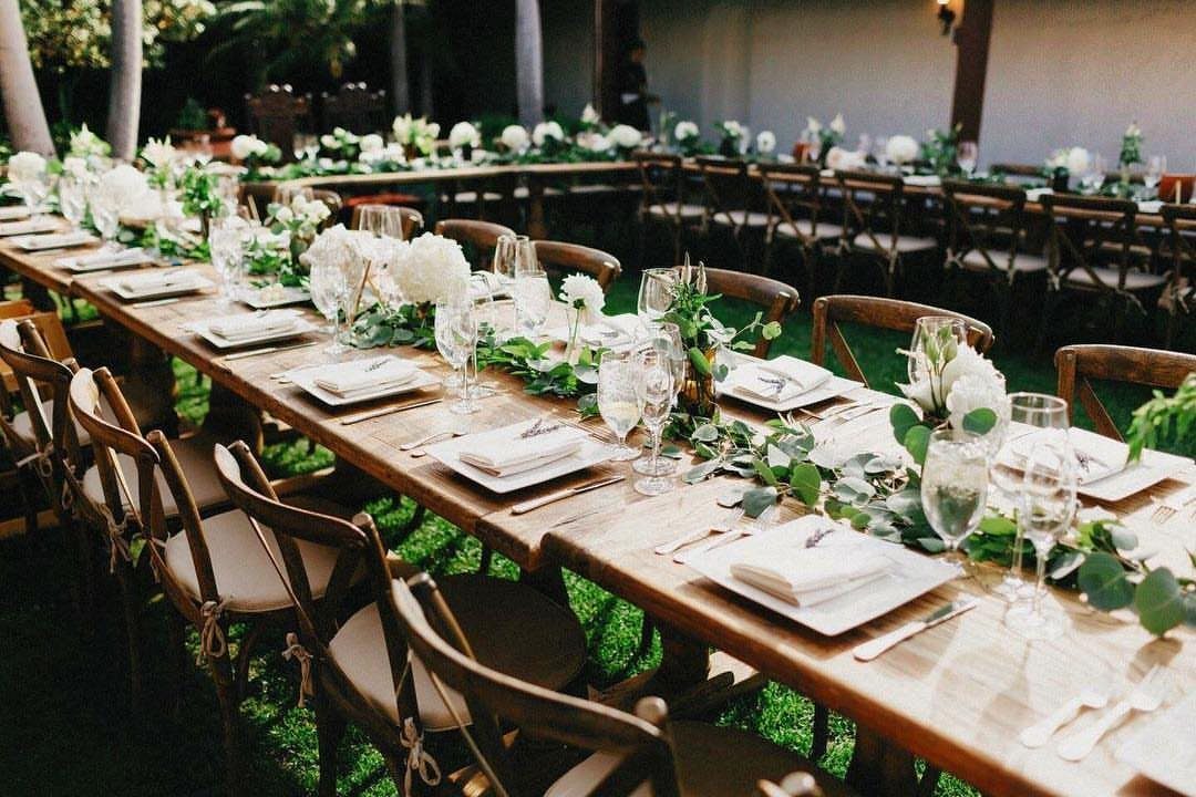 Long wooden banquet tables with white flowers and greenery for a family-style reception.