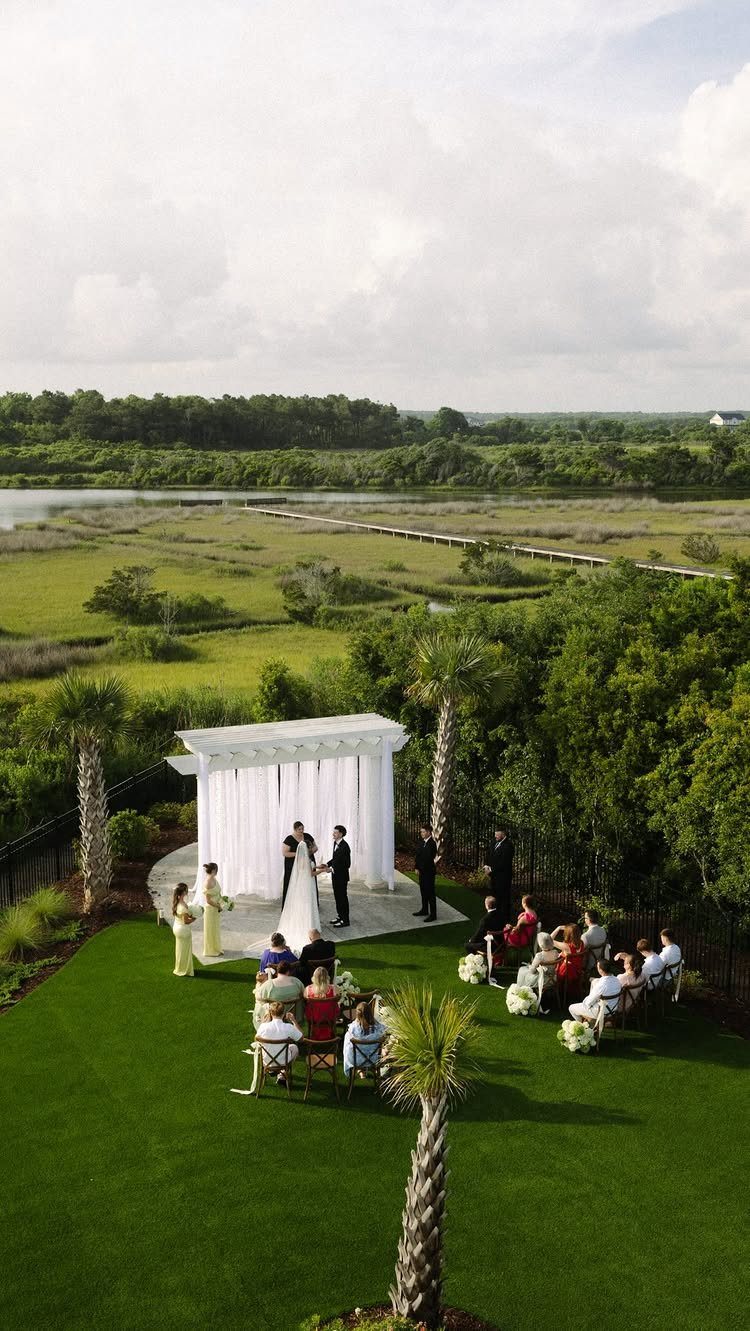 Small wedding ceremony under a white pergola on a lawn overlooking a marsh.