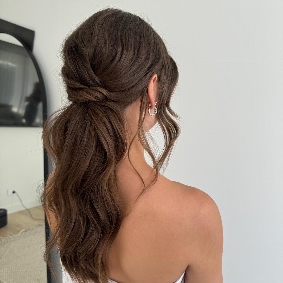 6 Side Ponytail Wedding Hairstyles for Every Bridal Look 2 Low romantic ponytail with wavy brown hair on a woman in white.