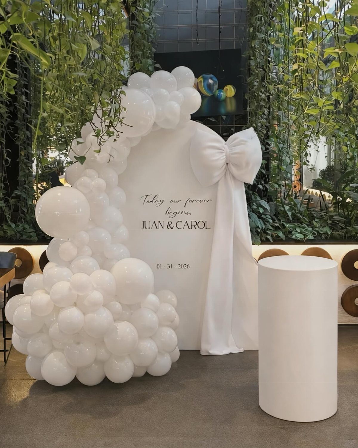 White wedding backdrop with a large fabric bow and organic white balloon garland.