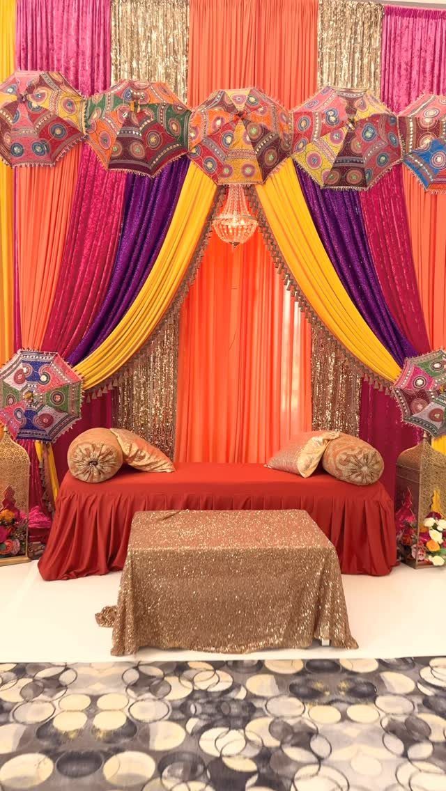 Colorful draped fabric backdrop with embroidered umbrellas and a red seating area.