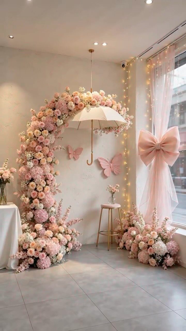Pink and cream rose floral arch with a hanging white umbrella and butterfly decorations.