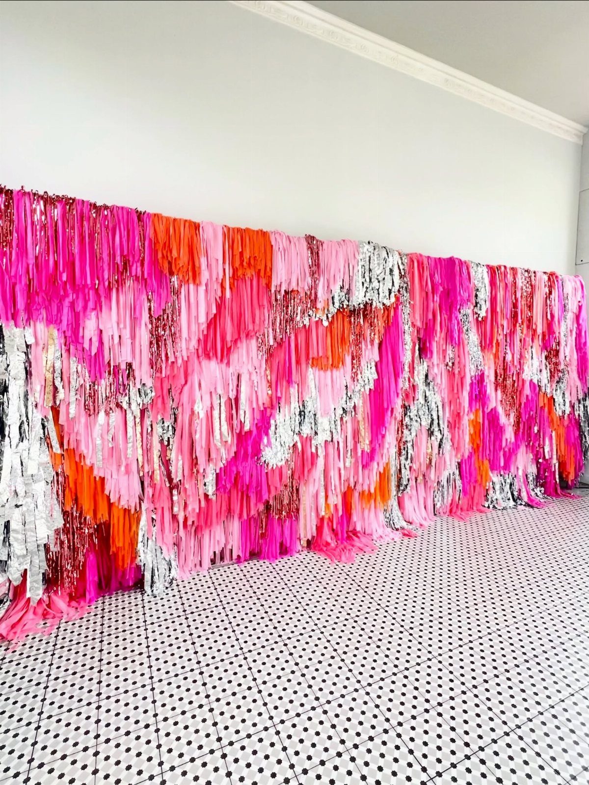 Colorful pink, orange, and silver fringe streamers covering a wall as a backdrop.