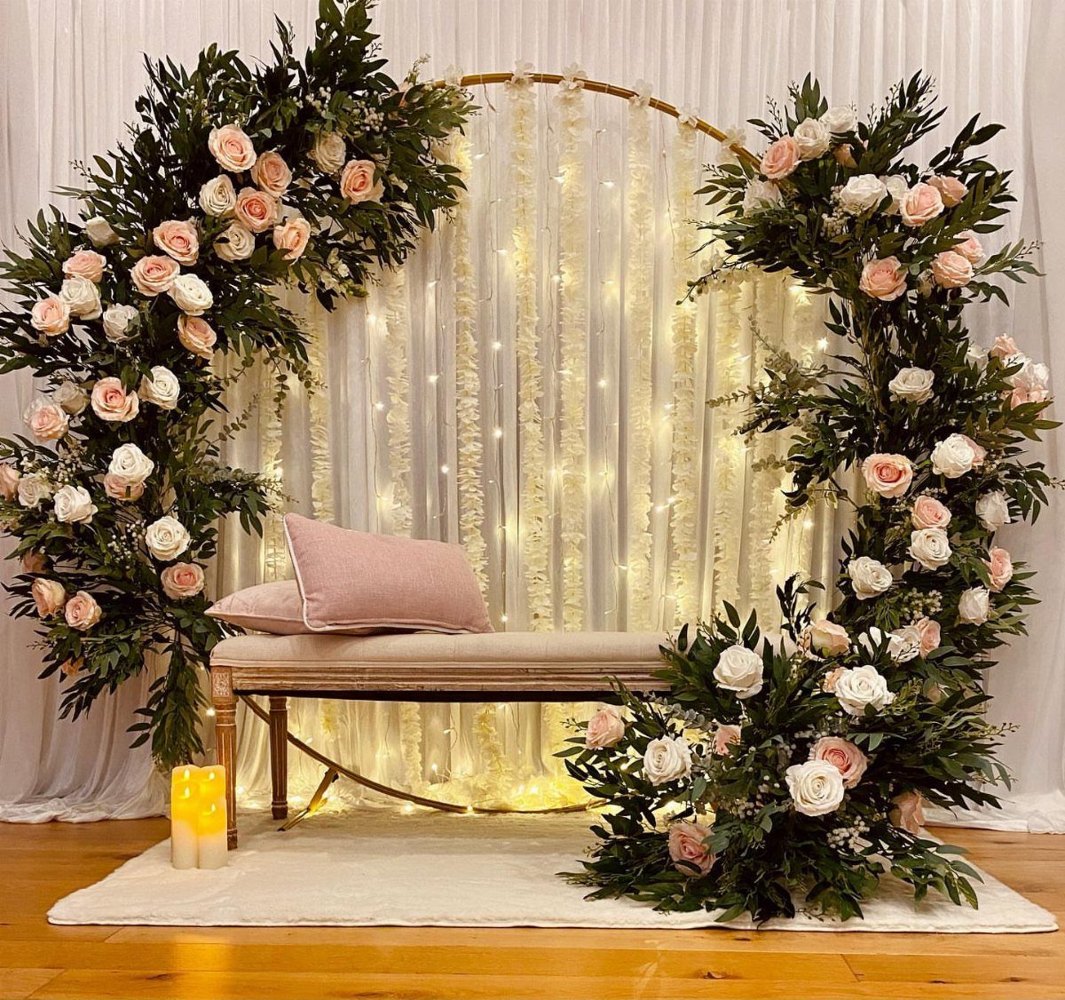 Circular gold hoop with pink roses and greenery in front of fairy lights.