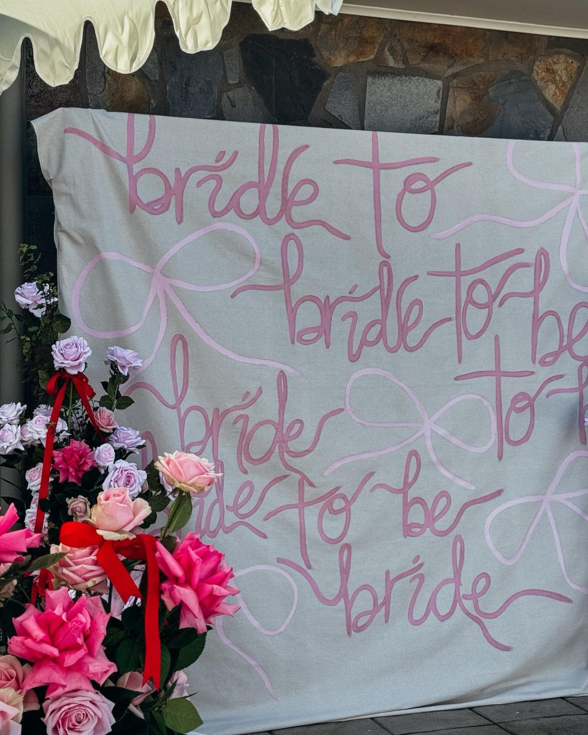 White canvas backdrop with pink bride to be lettering and pink roses.