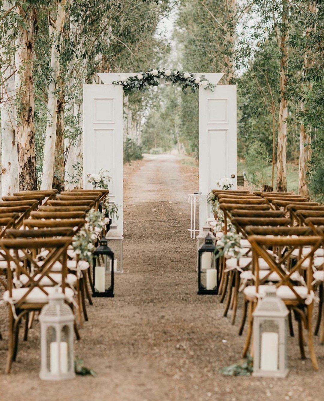 White vintage doors with a floral arch as a wedding backdrop in the woods.