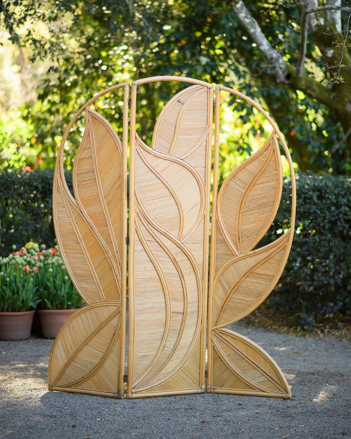Wicker room divider with leaf patterns standing outdoors in a garden setting.