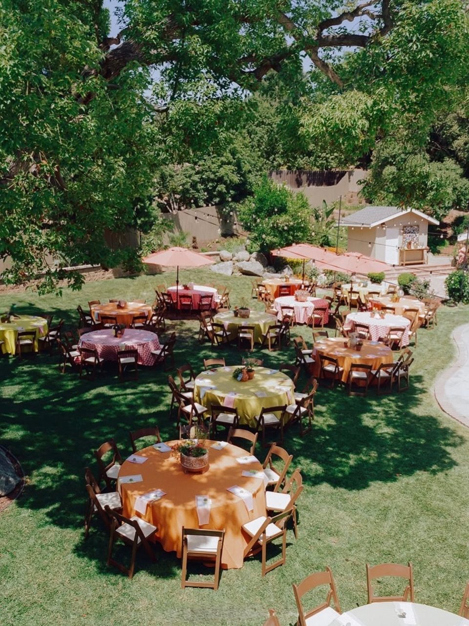 Round tables with colorful linens and wooden chairs in a sunny backyard garden.