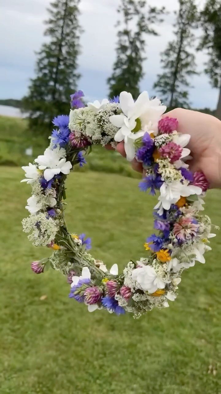 Flower crown made of colorful wildflowers held up against a grassy outdoor background.