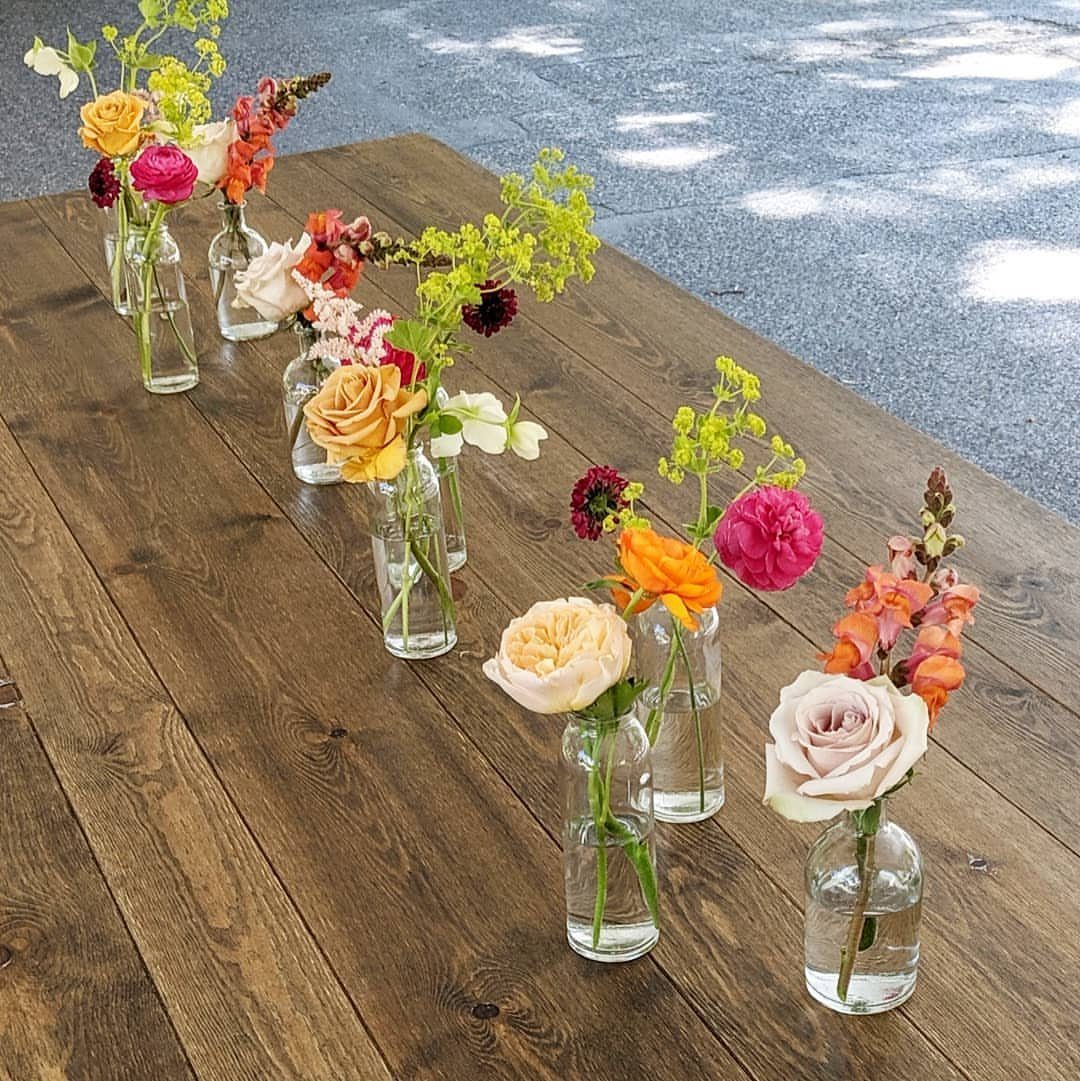 Colorful garden flowers in small glass bottles arranged on a rustic wooden table.
