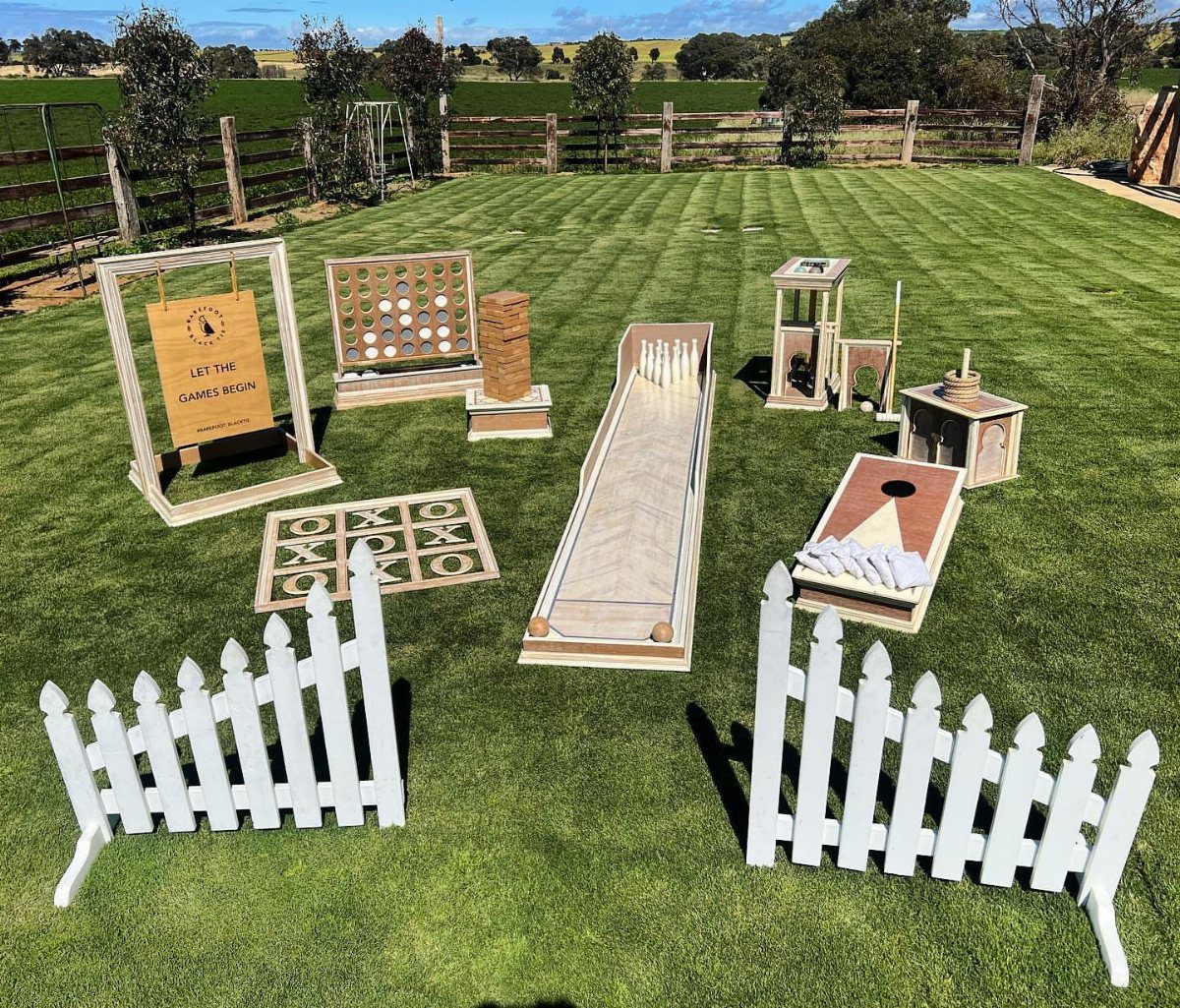 Wooden lawn games arranged on a green grass field behind a white picket fence.