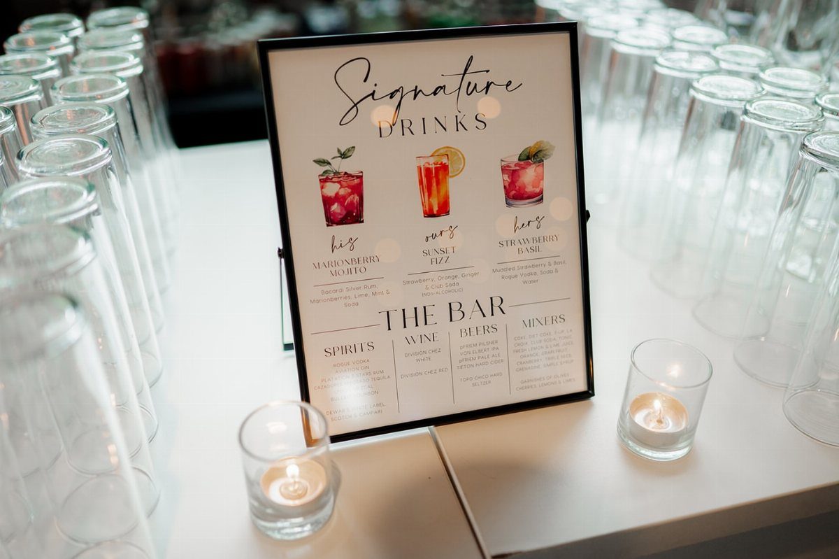 Signature drinks menu on a white table with empty glasses and lit candles.