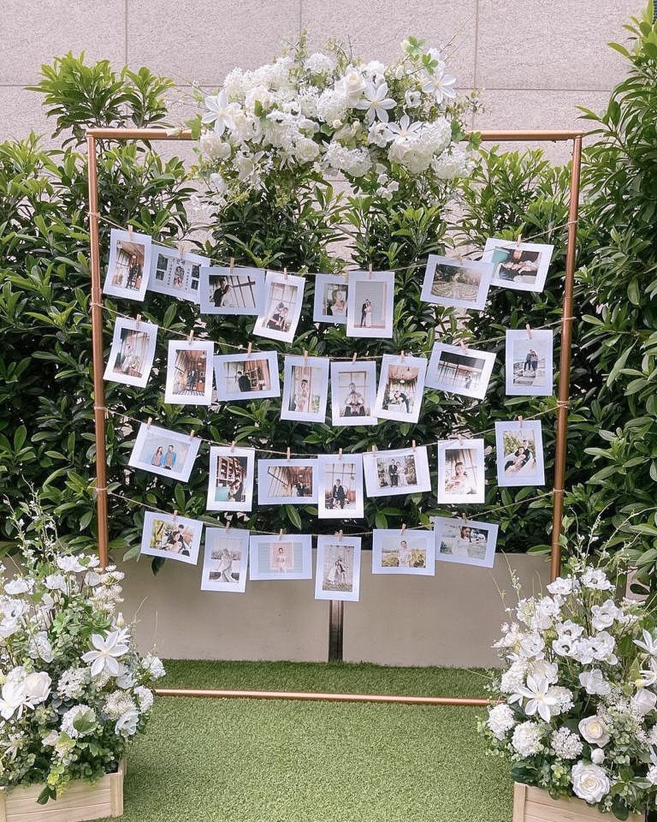 Wedding photo display with pictures clipped to strings on a gold floral frame.