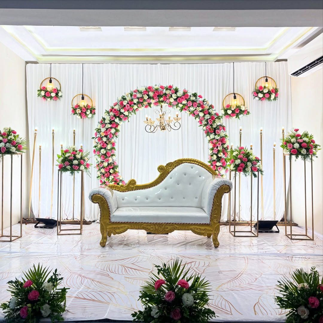 Ornate white sofa on a stage with a pink floral arch and white curtains.