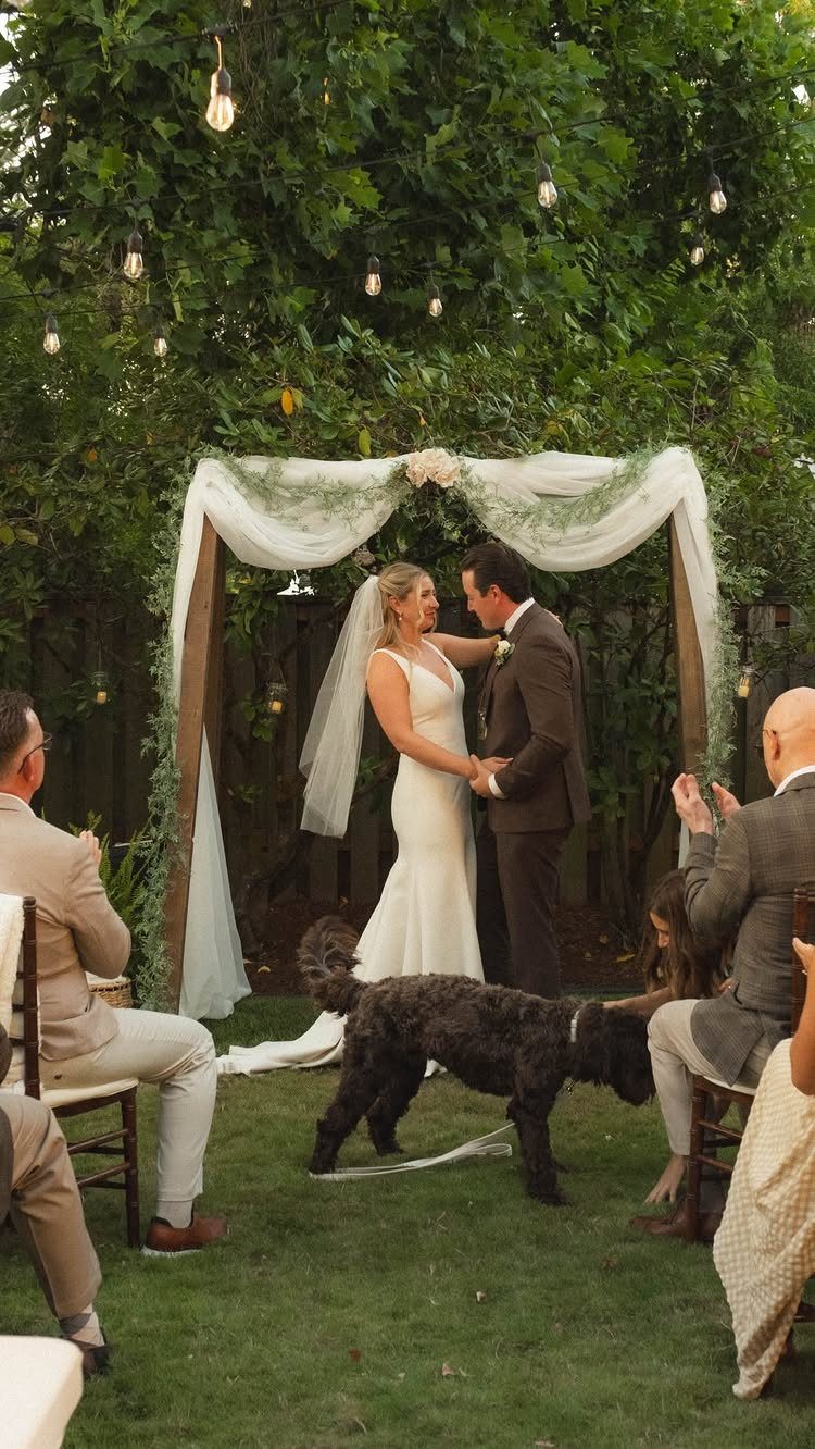 Bride and groom standing under a simple fabric draped arch at an outdoor wedding