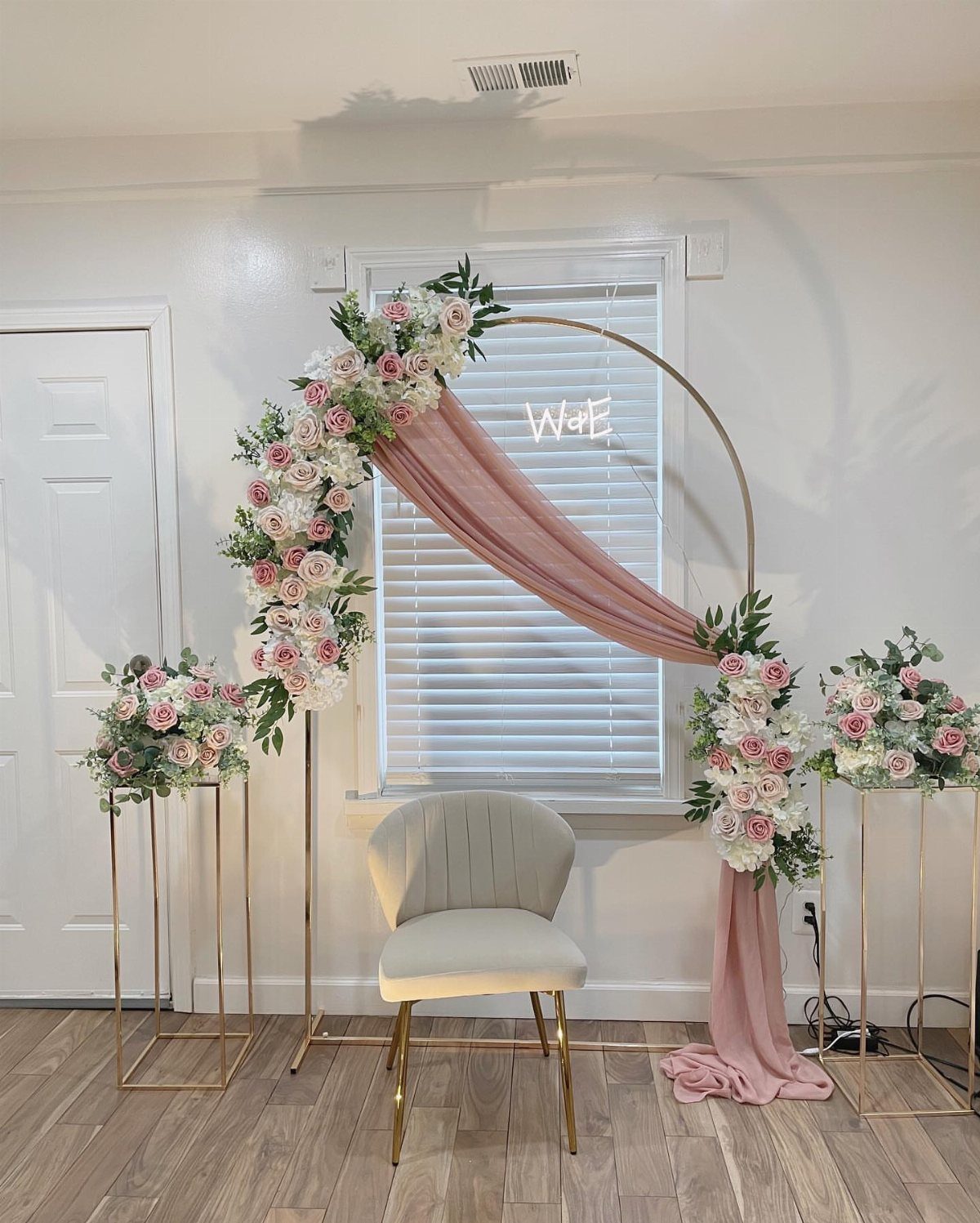 Gold circular wedding arch with pink fabric draping, roses, and a neon sign.