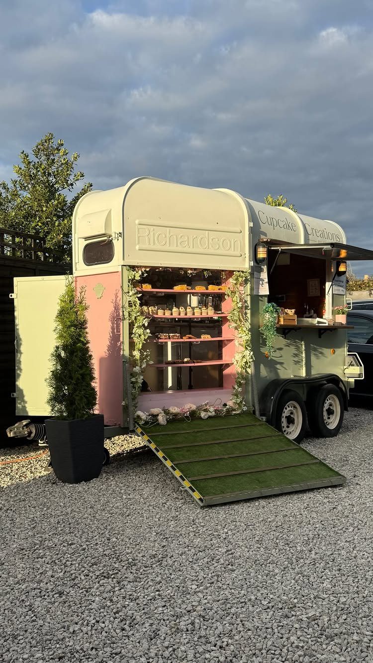 Pastel green and pink vintage food truck decorated with flowers on gravel.