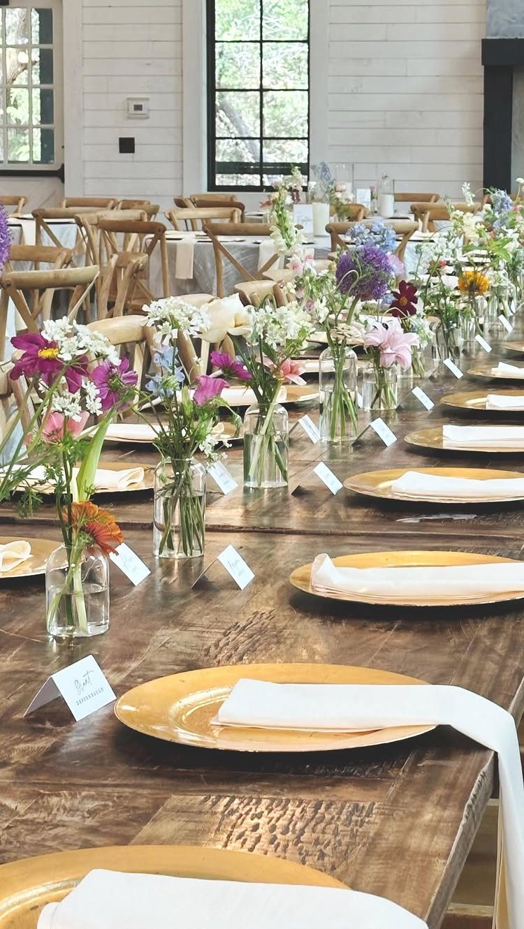 Gold charger plates and white napkins on a wooden table with wildflower centerpieces.