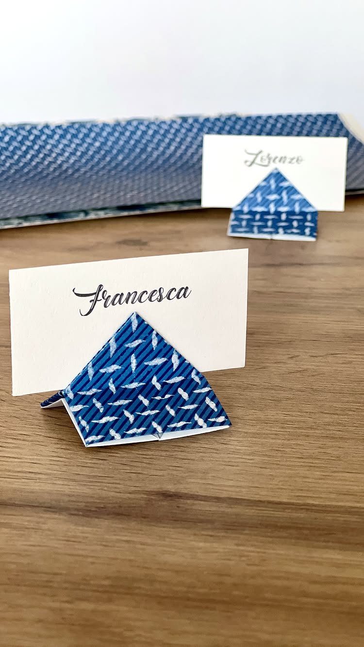 White place cards with cursive names held by blue patterned paper holders on wood.