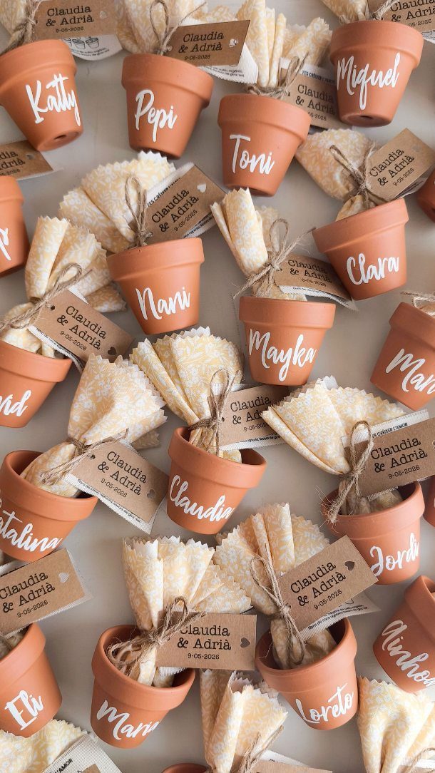 Terracotta pots with white napkins and personalized name tags for wedding guests.