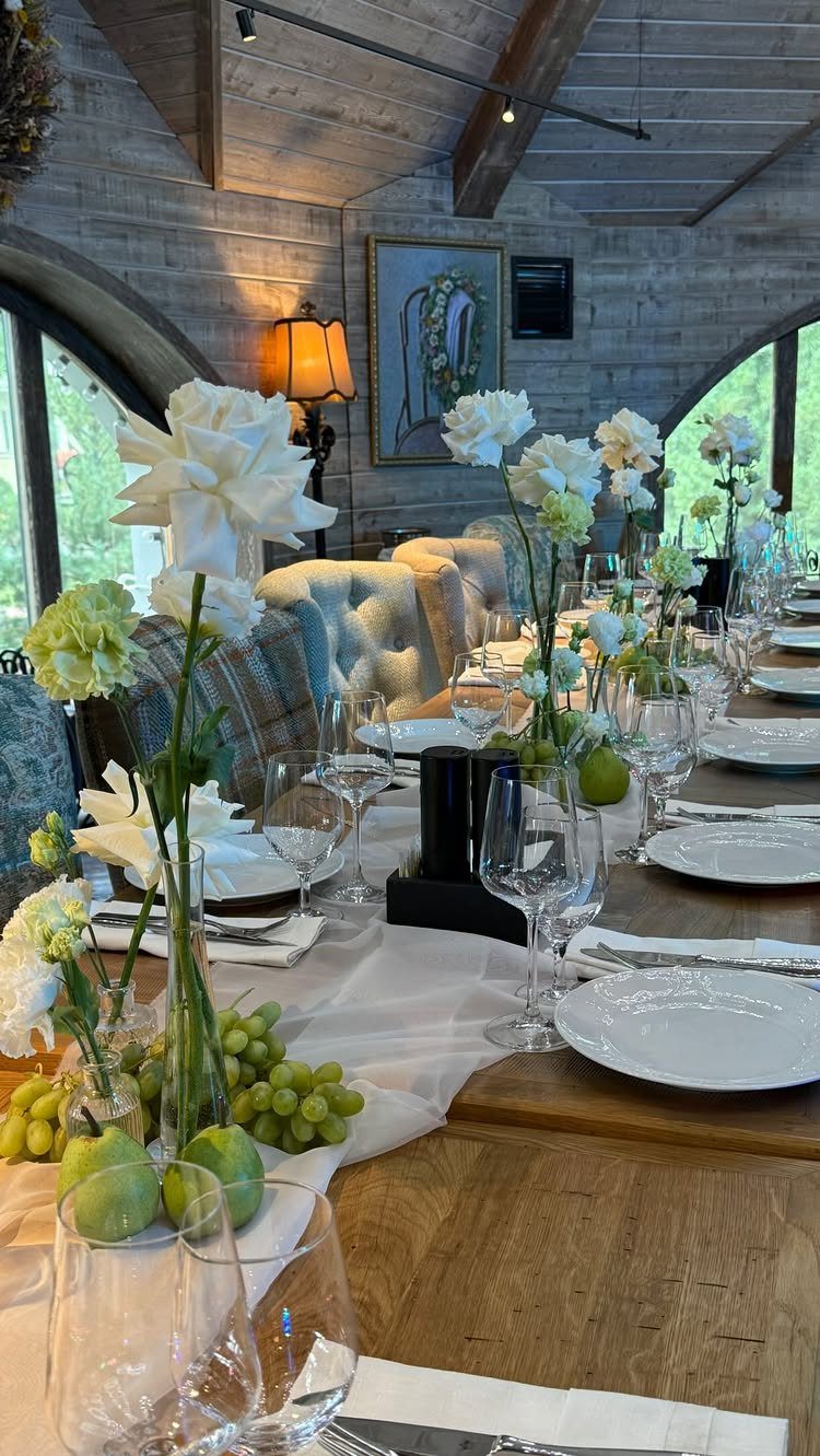 Wooden wedding table featuring white floral centerpieces accented with green grapes and apples.