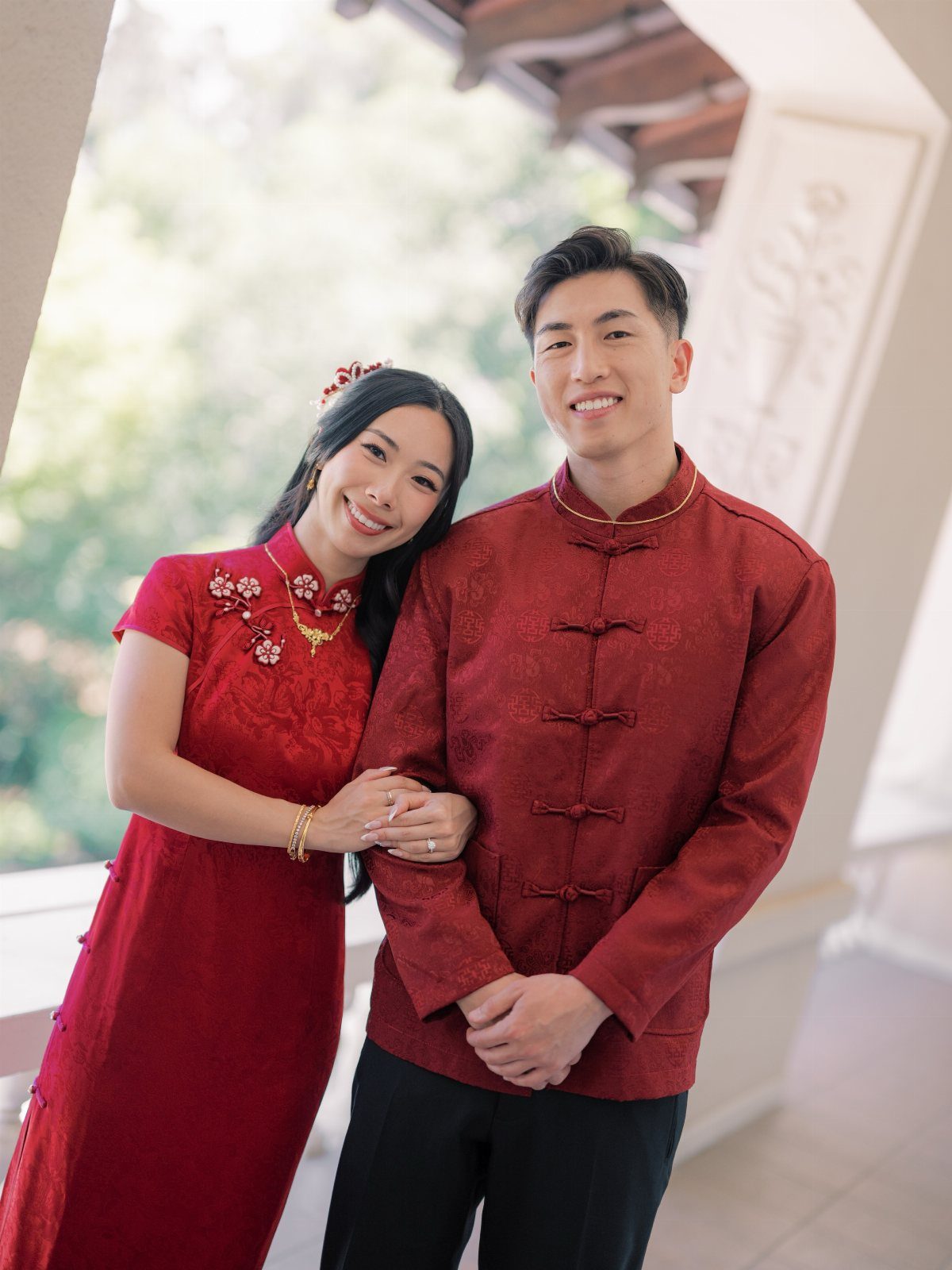 15 Small Wedding Ideas for 50 Guests, From Backyards to Parks 9 Couple wearing traditional red Chinese wedding attire posing together on a balcony.
